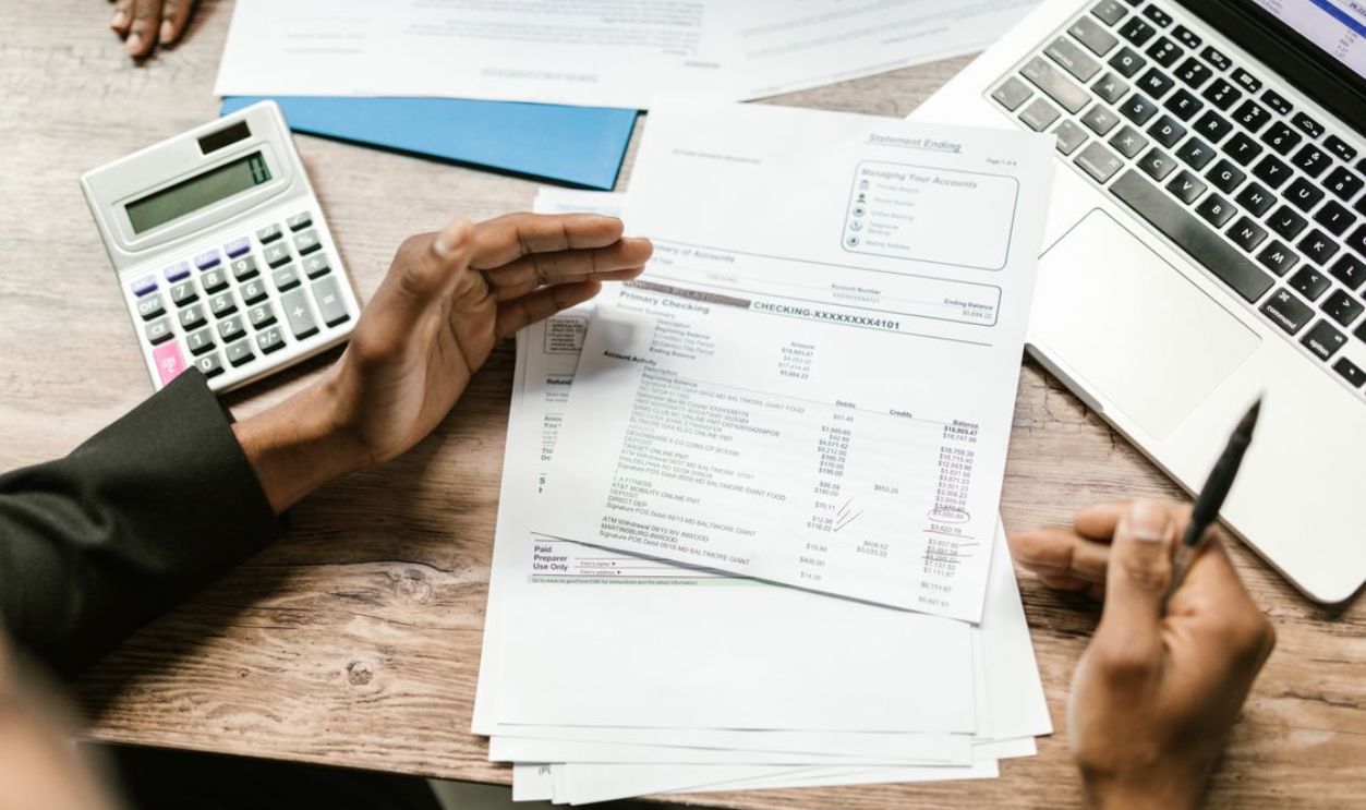Hands holding financial documents with calculator and laptop on office desk, business analysis scene