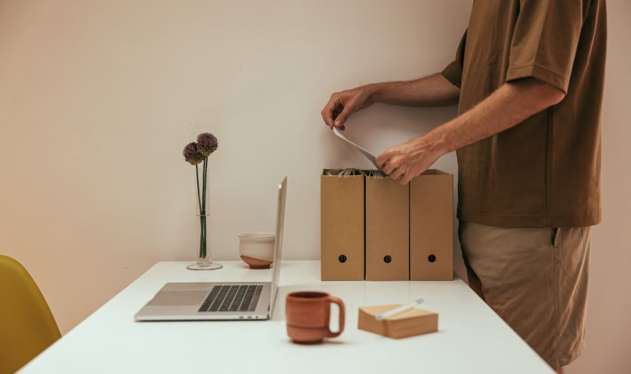 Man organizing papers in a minimal home office with white table and laptop