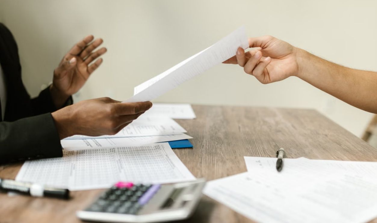 Two professionals exchanging documents in a corporate setting, emphasizing collaboration and paperwork