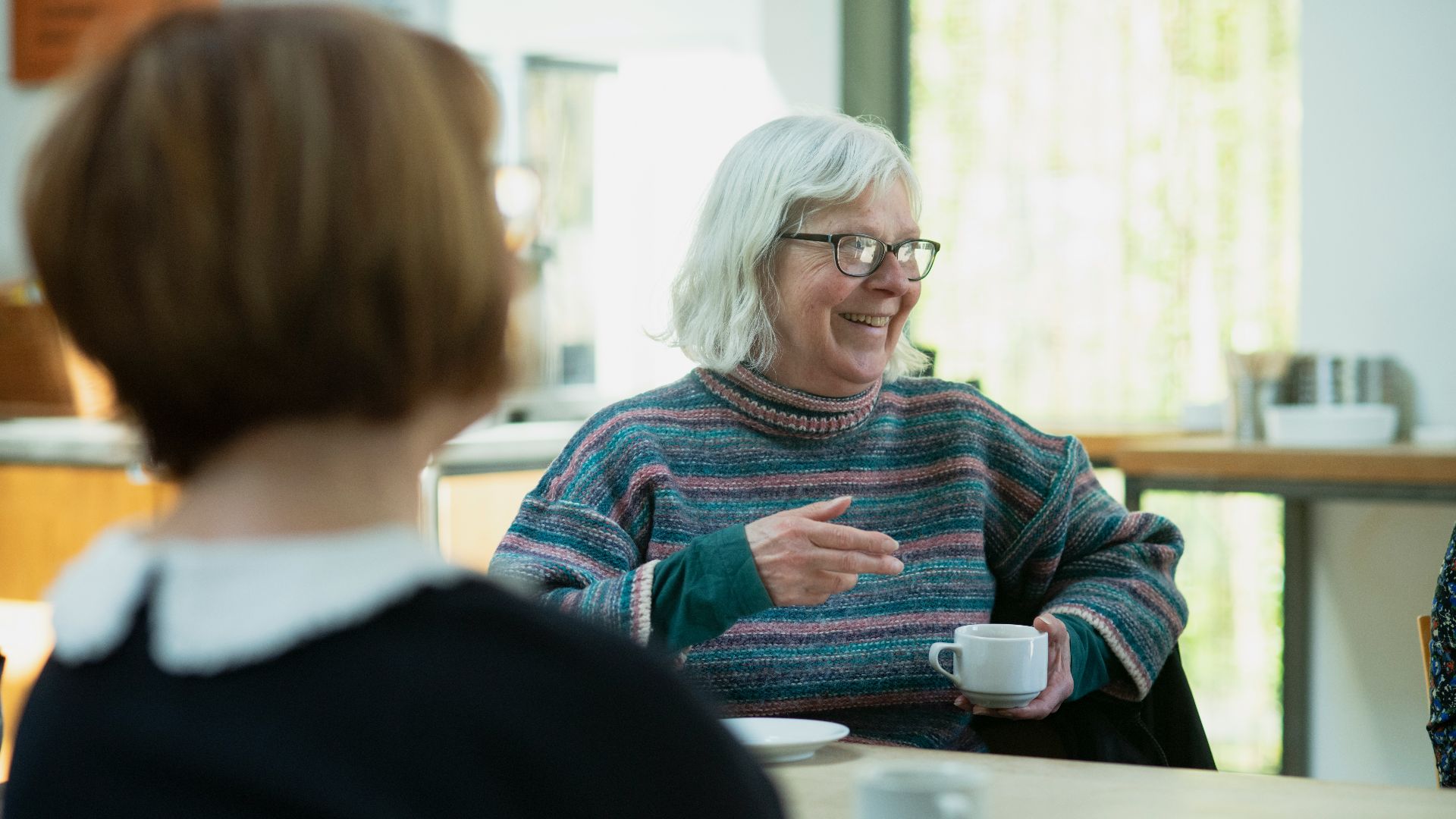 a woman sitting at a table talking to another woman