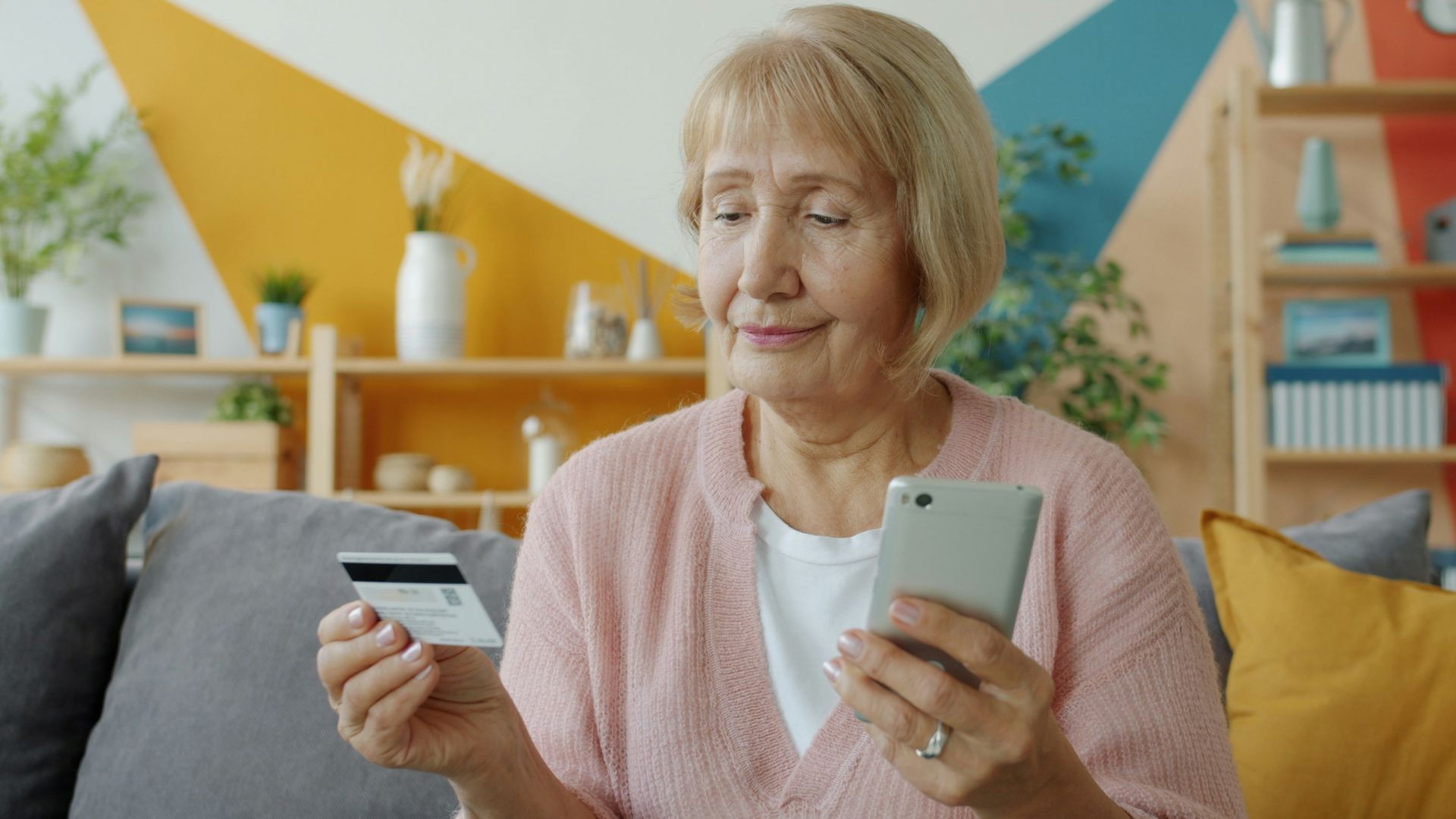 Elderly woman holding credit card and smartphone.