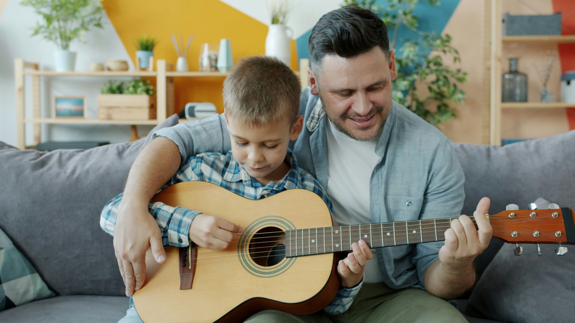Father and son playing guitar together on couch.