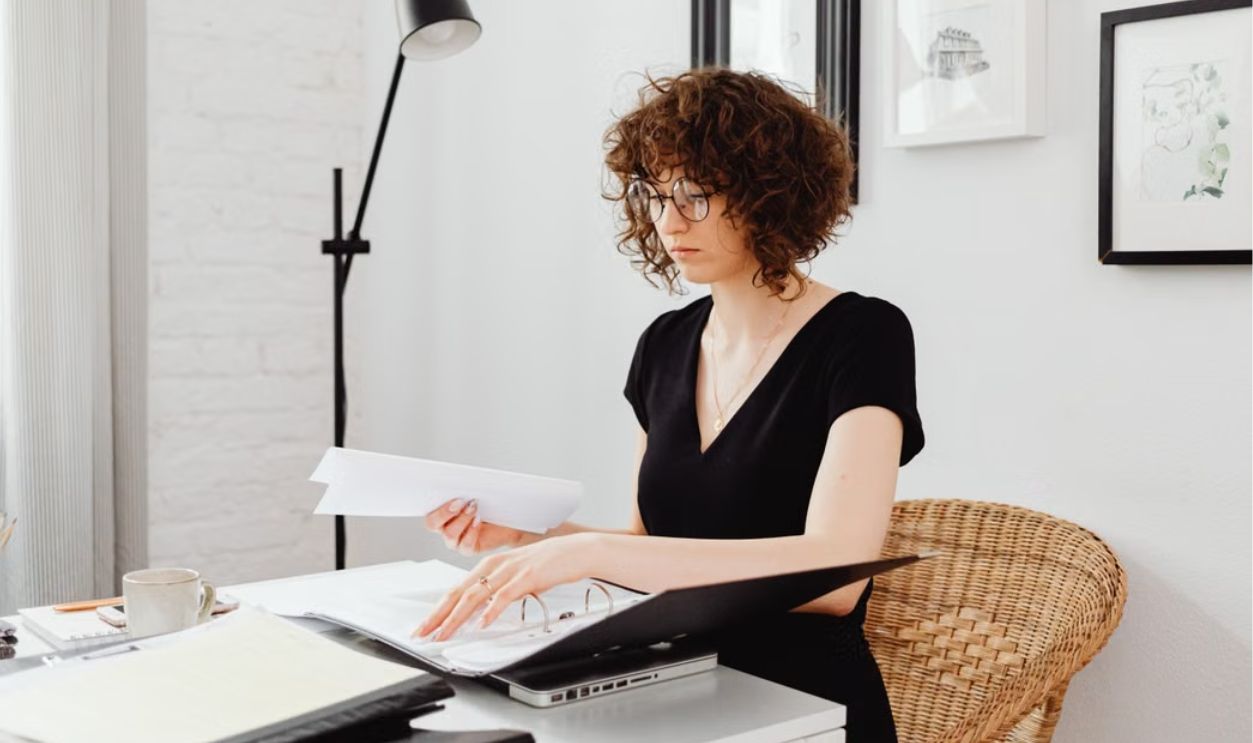 Caucasian woman with curly hair working at home office desk, organizing documents