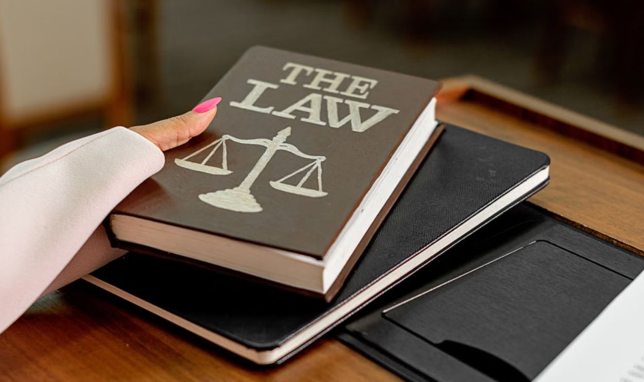Closeup image of a law book titled 'The Law' on a wooden desk with scales of justice.