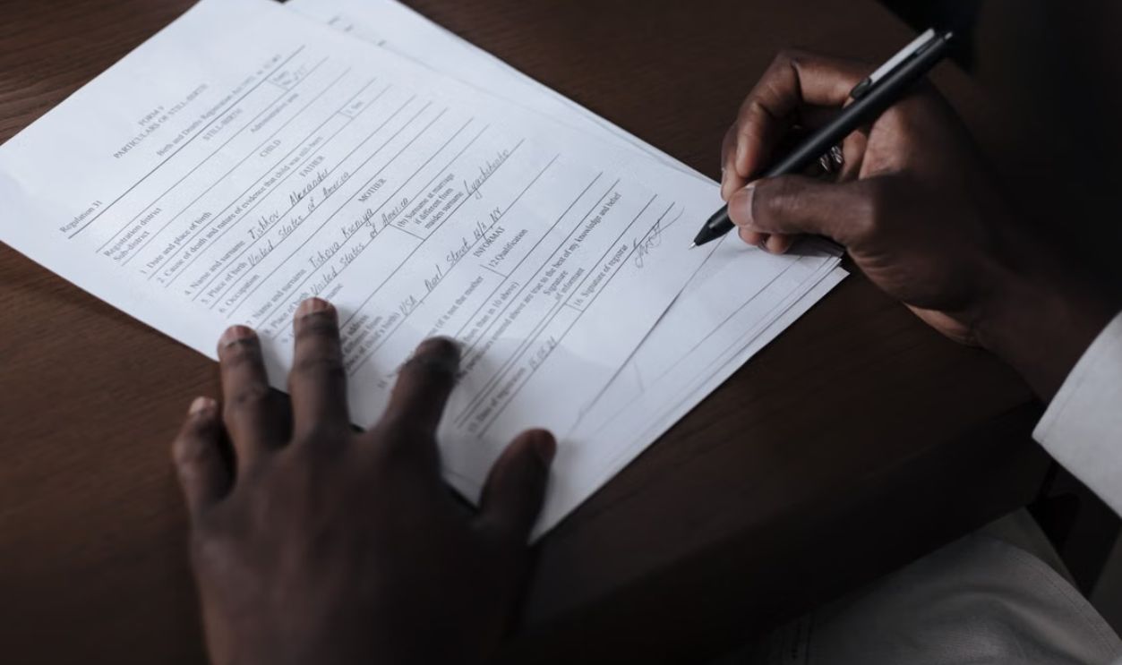 A detailed view of a man signing official documents with a pen at a table.