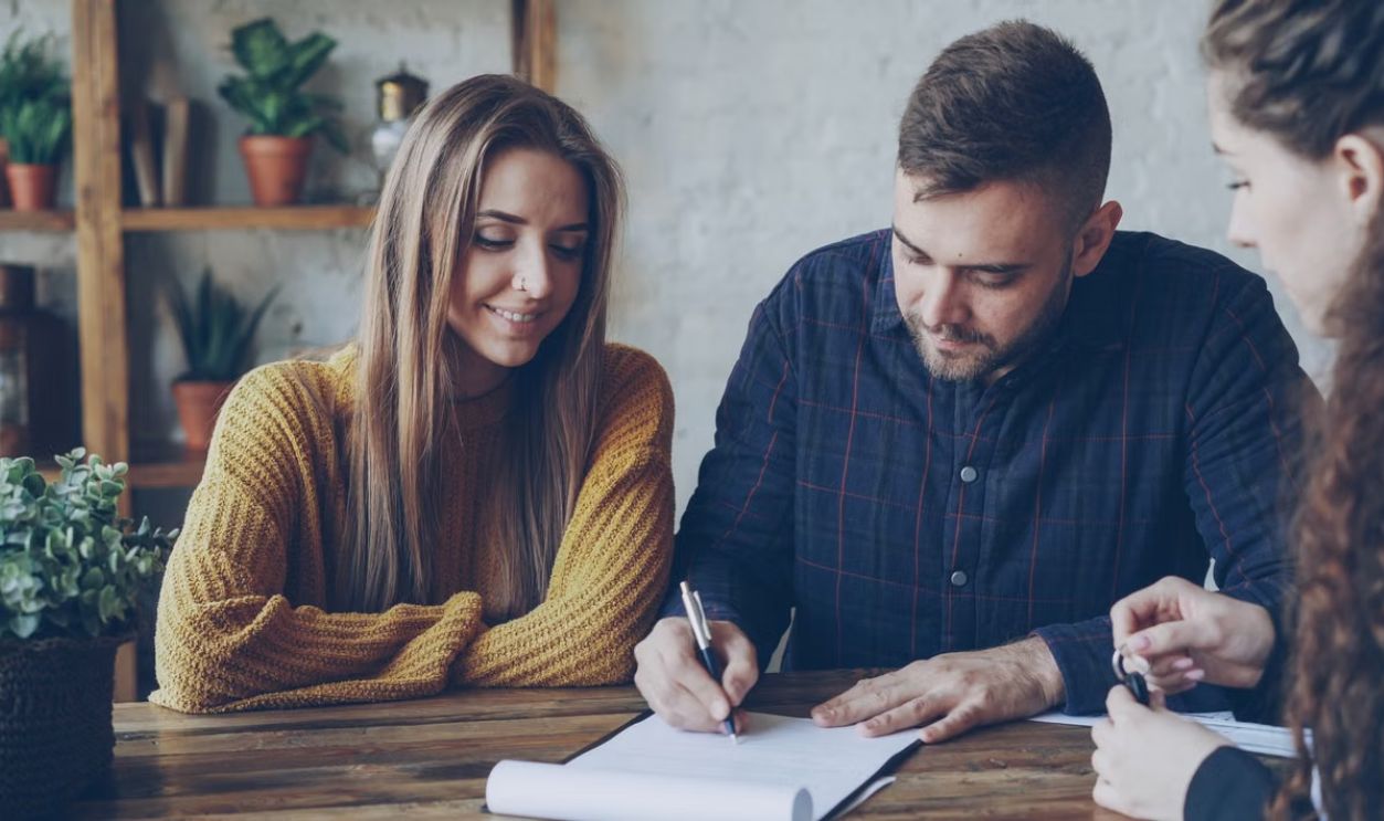 Three adults in a casual office setting reviewing and signing documents.