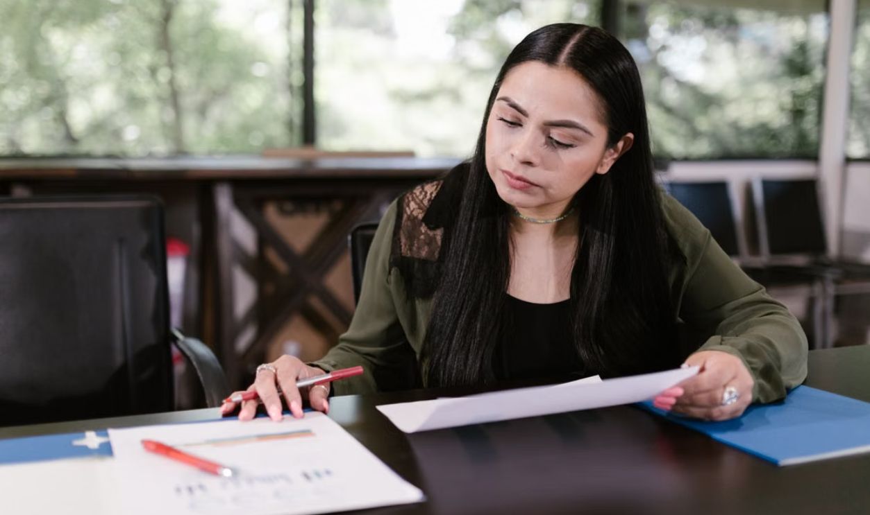 Professional woman in office setting studying documents with concentration.