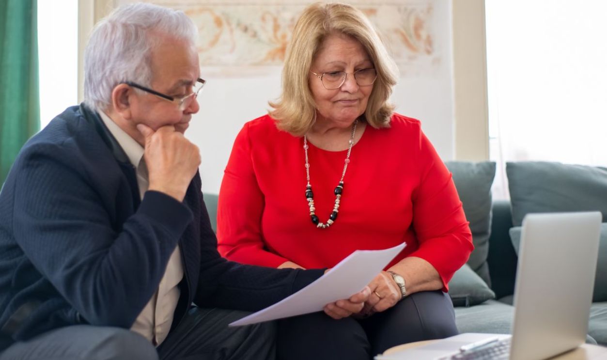Elderly couple reviewing financial documents together at home in Portugal.