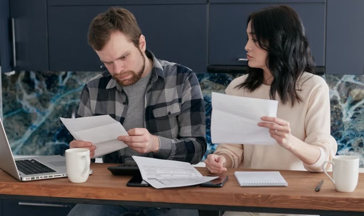 A young couple sits at home looking at financial documents with concern.