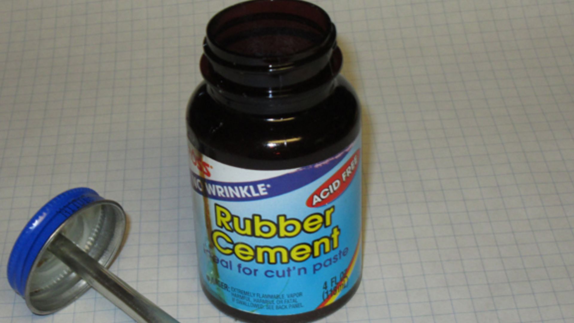 Bottle of rubber cement, showing rubber cement-filled brush built into the cap, and a photo about to be cemented to graph paper.