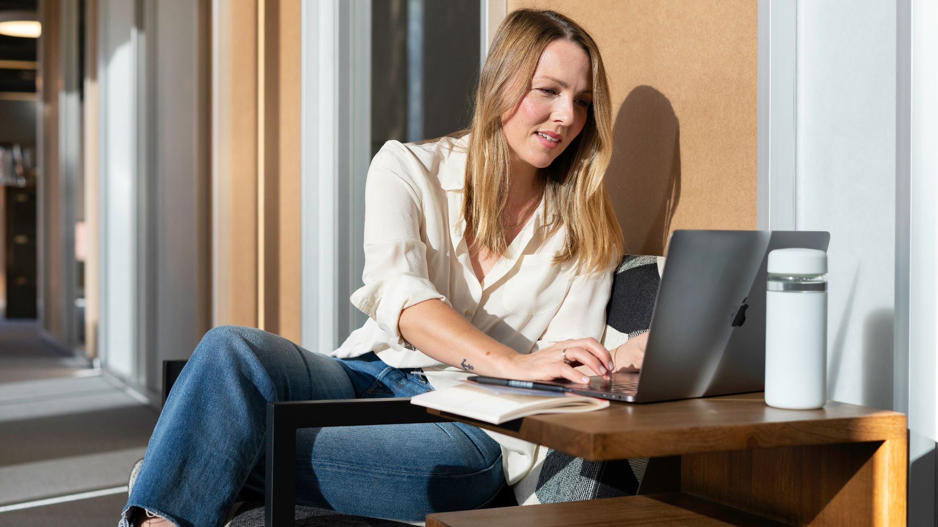 woman in white long sleeve shirt and blue denim jeans sitting on brown wooden table using
