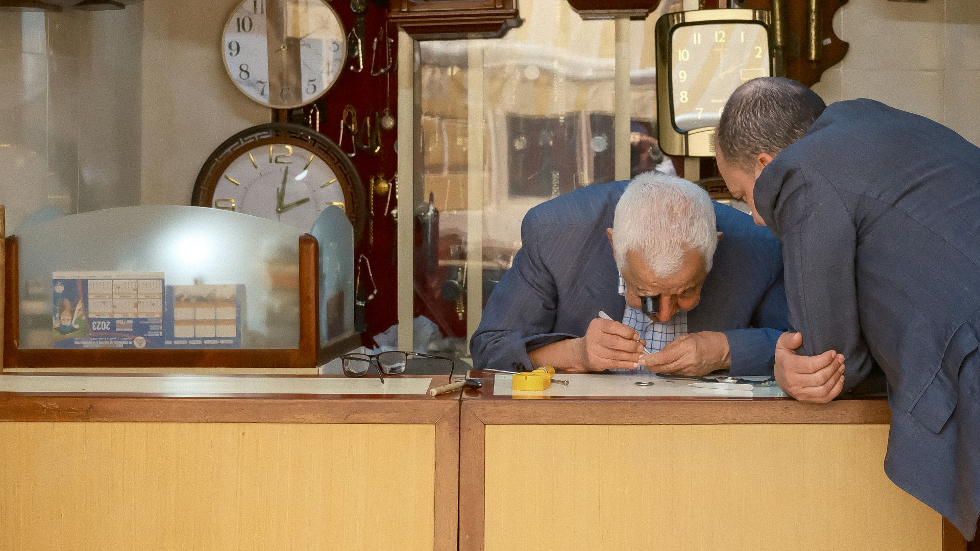 Two men examining a small object in a clock shop.