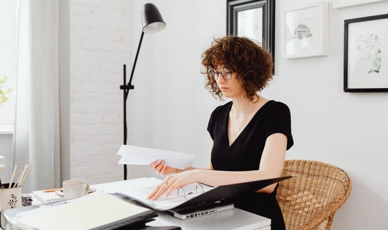 Caucasian woman with curly hair working at home office desk, organizing documents