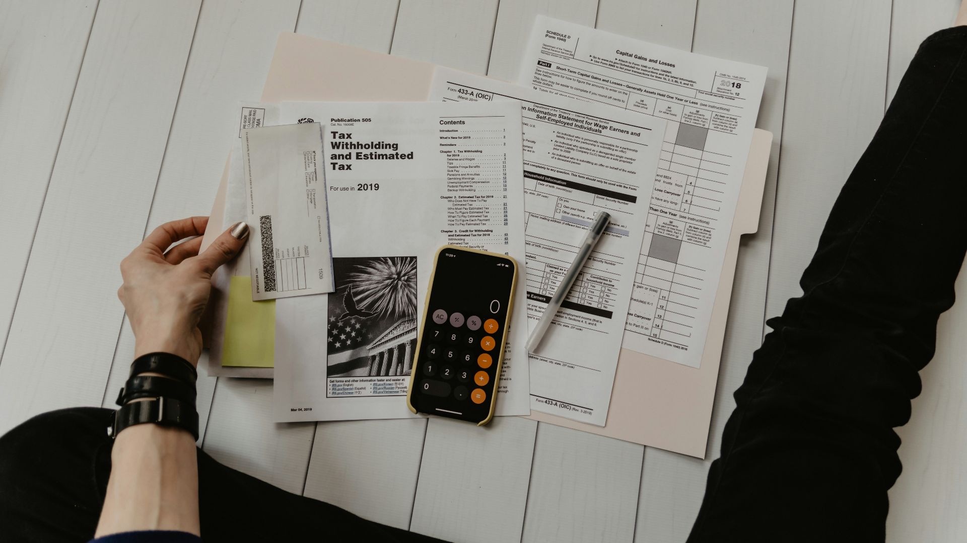 person holding paper near pen and calculator