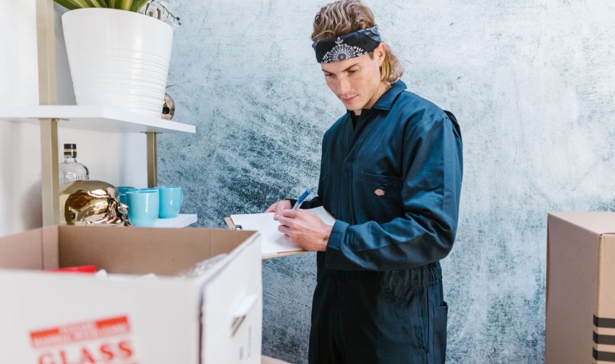 Man wearing overalls and bandana preparing for a home move, surrounded by boxes and fragile items.
