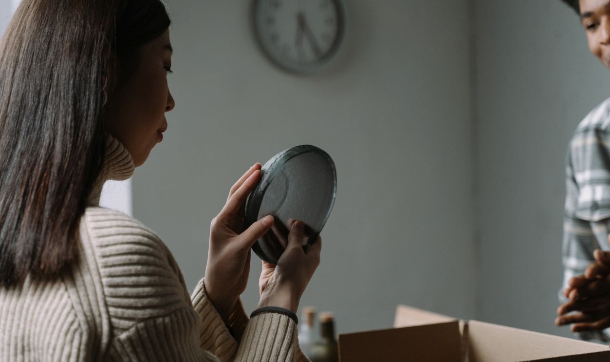 A woman carefully unpacks dishware from a cardboard box in a cozy indoor setting