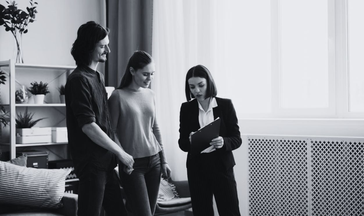 A young couple discusses home buying options with a real estate agent inside a well-lit modern room
