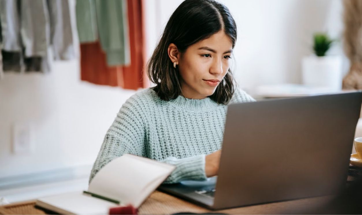 A young woman in a cozy room working on a laptop, showing concentration and dedication.