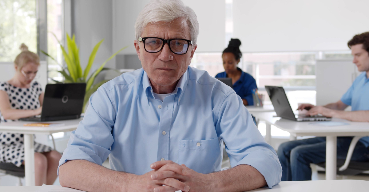 Senior manager sitting at desk in office with diverse colleagues working on background