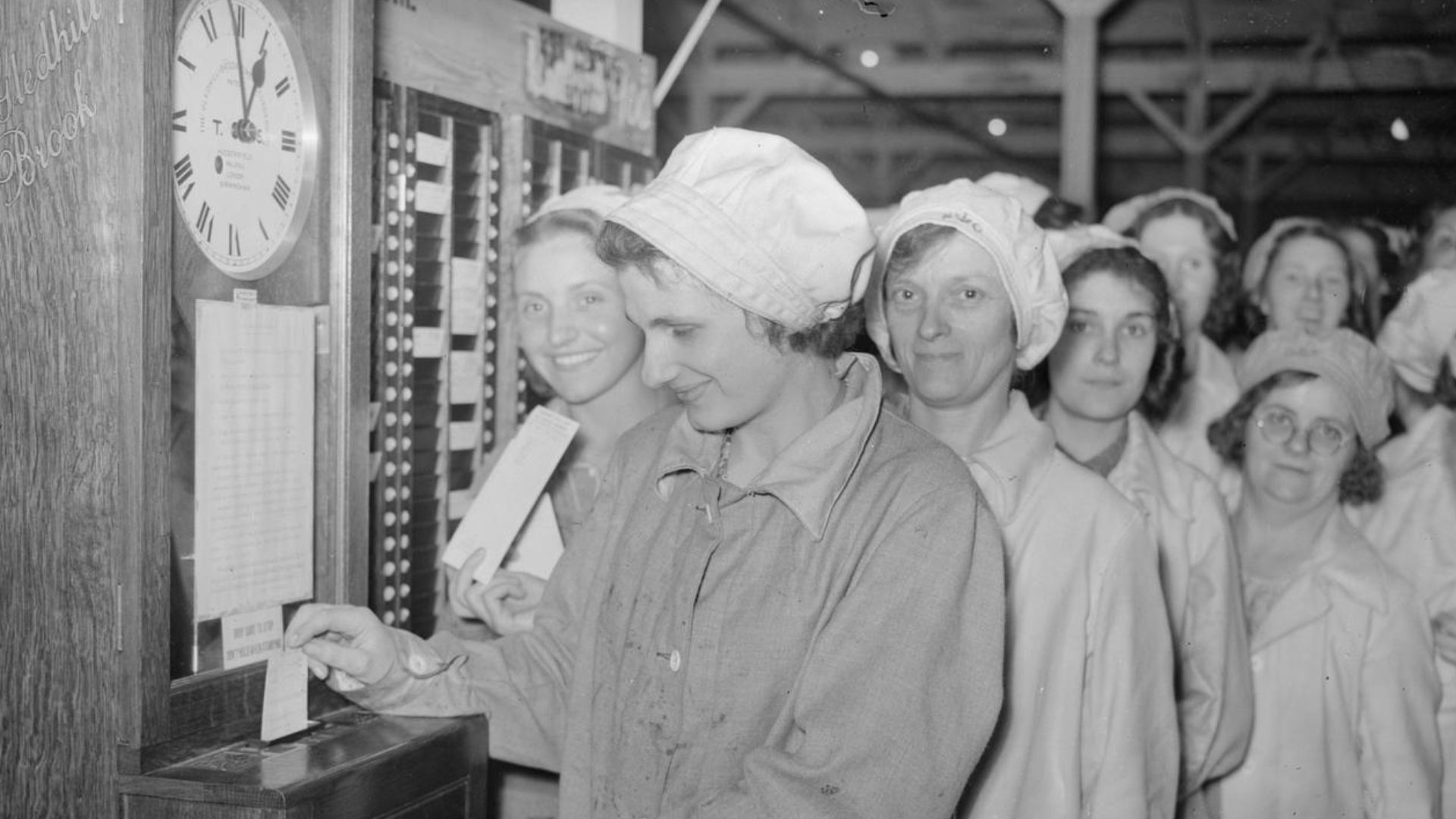 A Day in the Life of a Munitions Worker, Britain, 1940
Mrs Skinner clocks on for her shift at a munitions factory, somewhere in Britain, 1940.  A large group of her fellow workers are lined up behind her to punch their work card when their turn arrives.