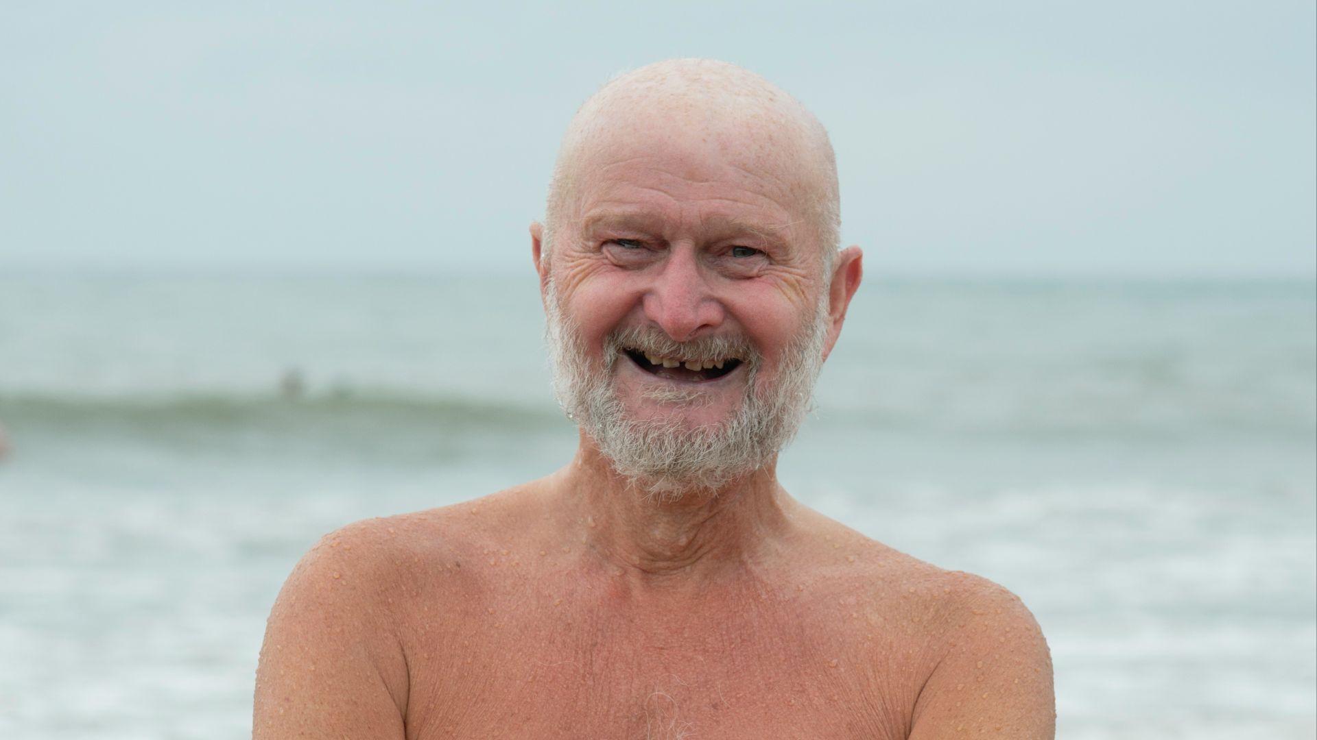 an older man standing on the beach with his arms crossed