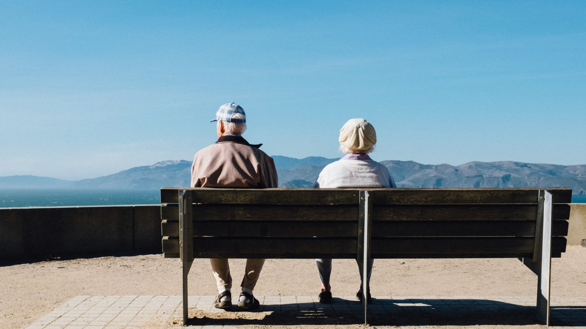 man and woman sitting on bench facing sea