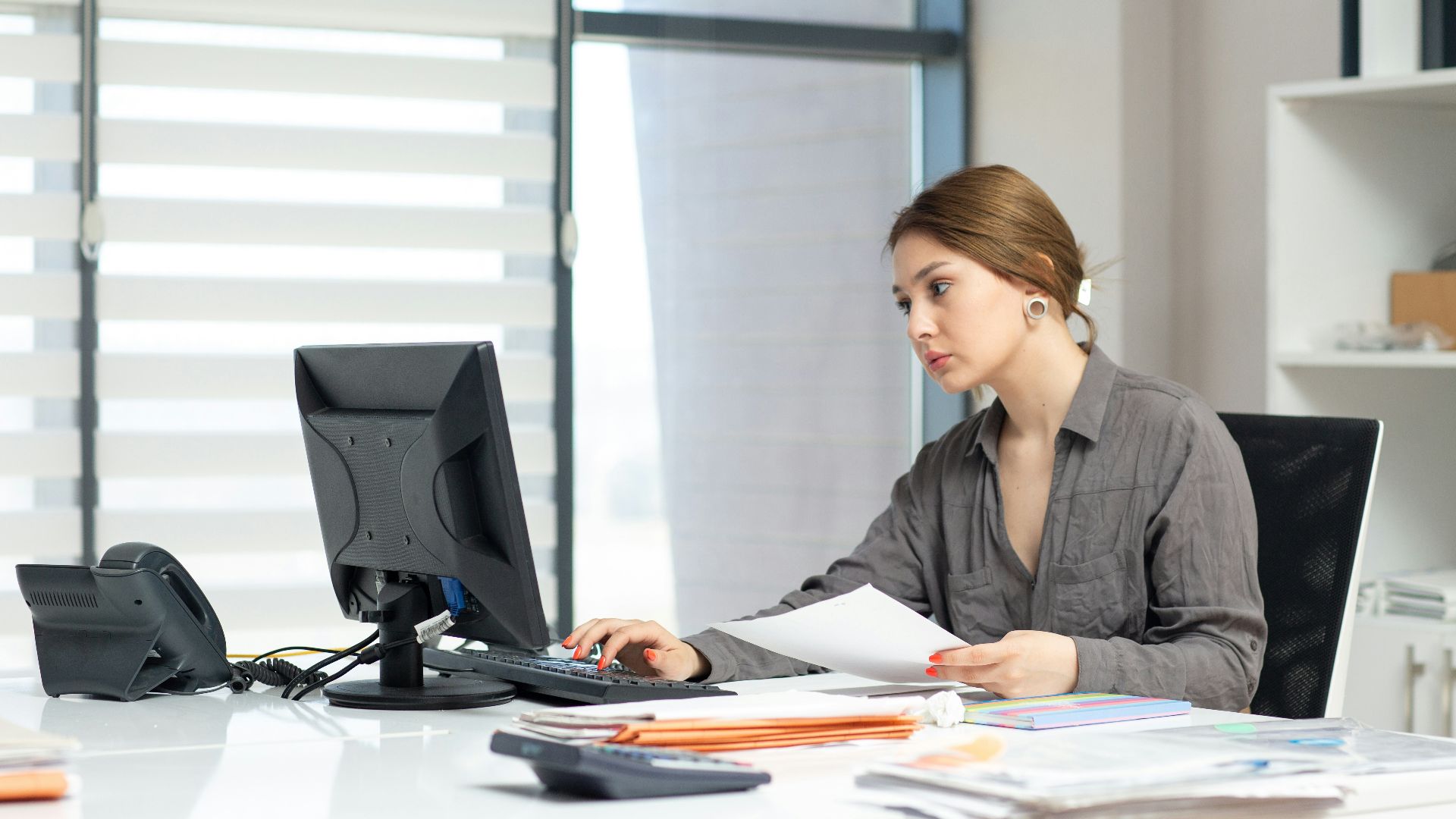 Young woman focused on computer and documents at office desk.