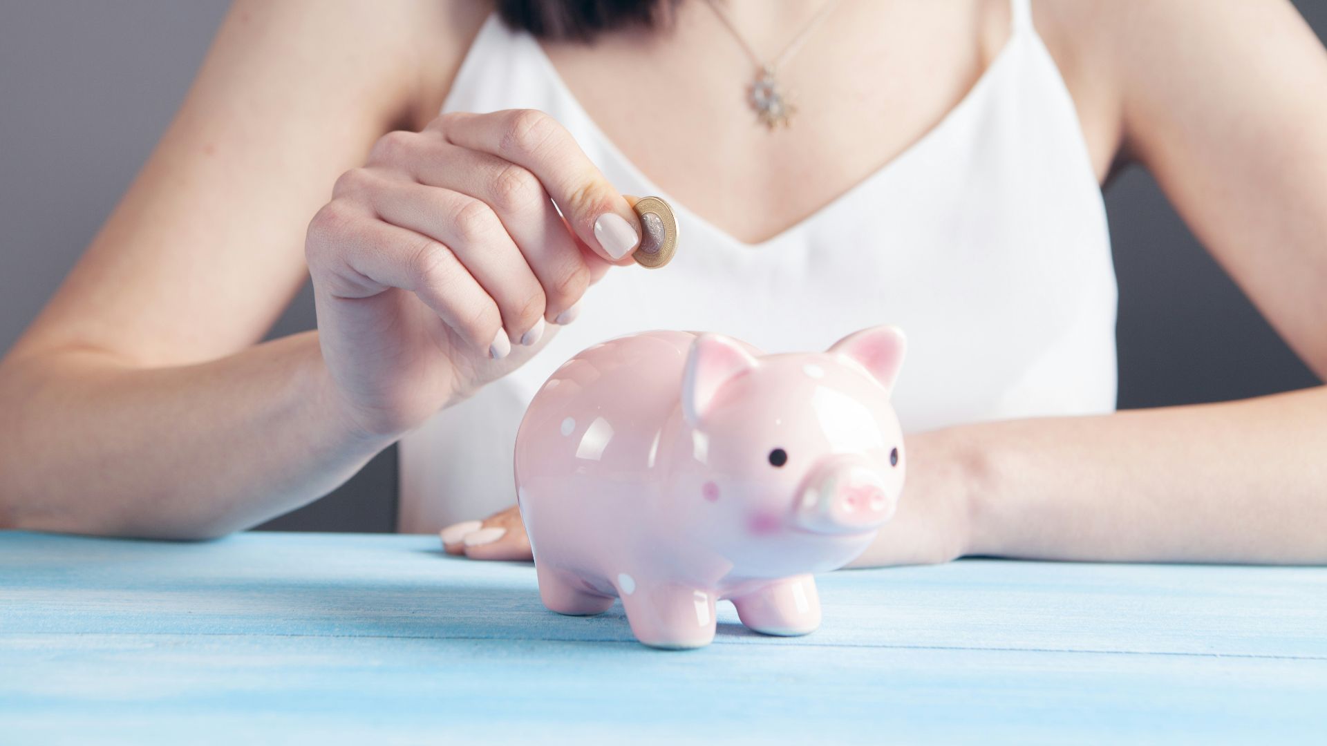 woman in white tank top holding pink pig figurine