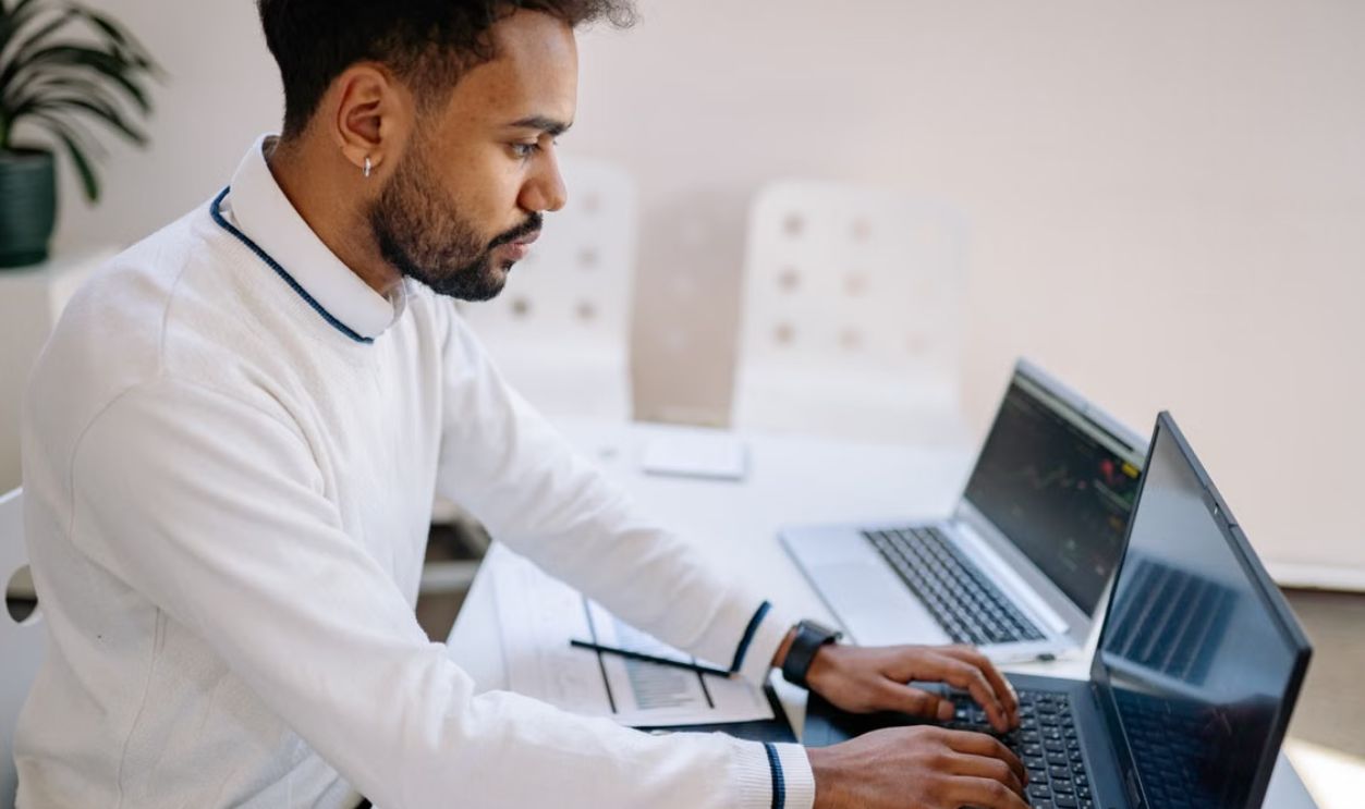 Young professional working diligently on multiple laptops in a modern office setting.