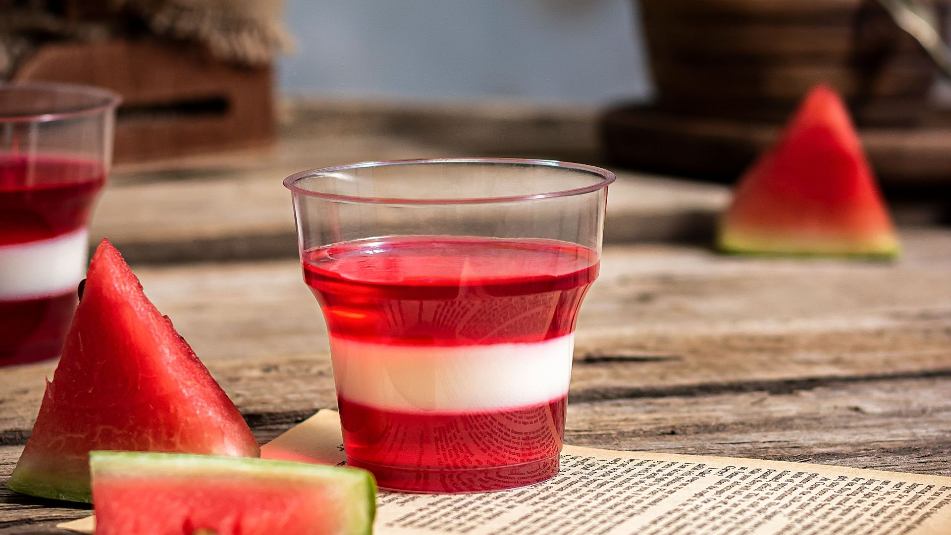 Close-up of watermelon jelly dessert in glass cups on a rustic wooden table, accompanied by slices of fresh watermelon.