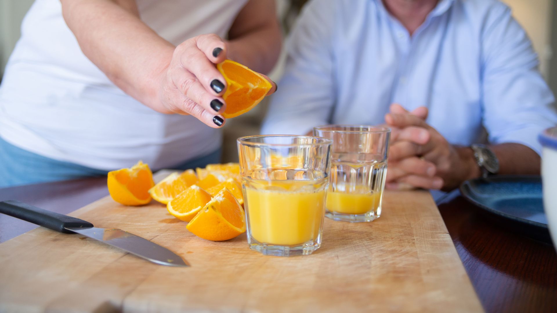 A person preparing fresh orange juice on a chopping board indoors, showcasing healthy lifestyle.