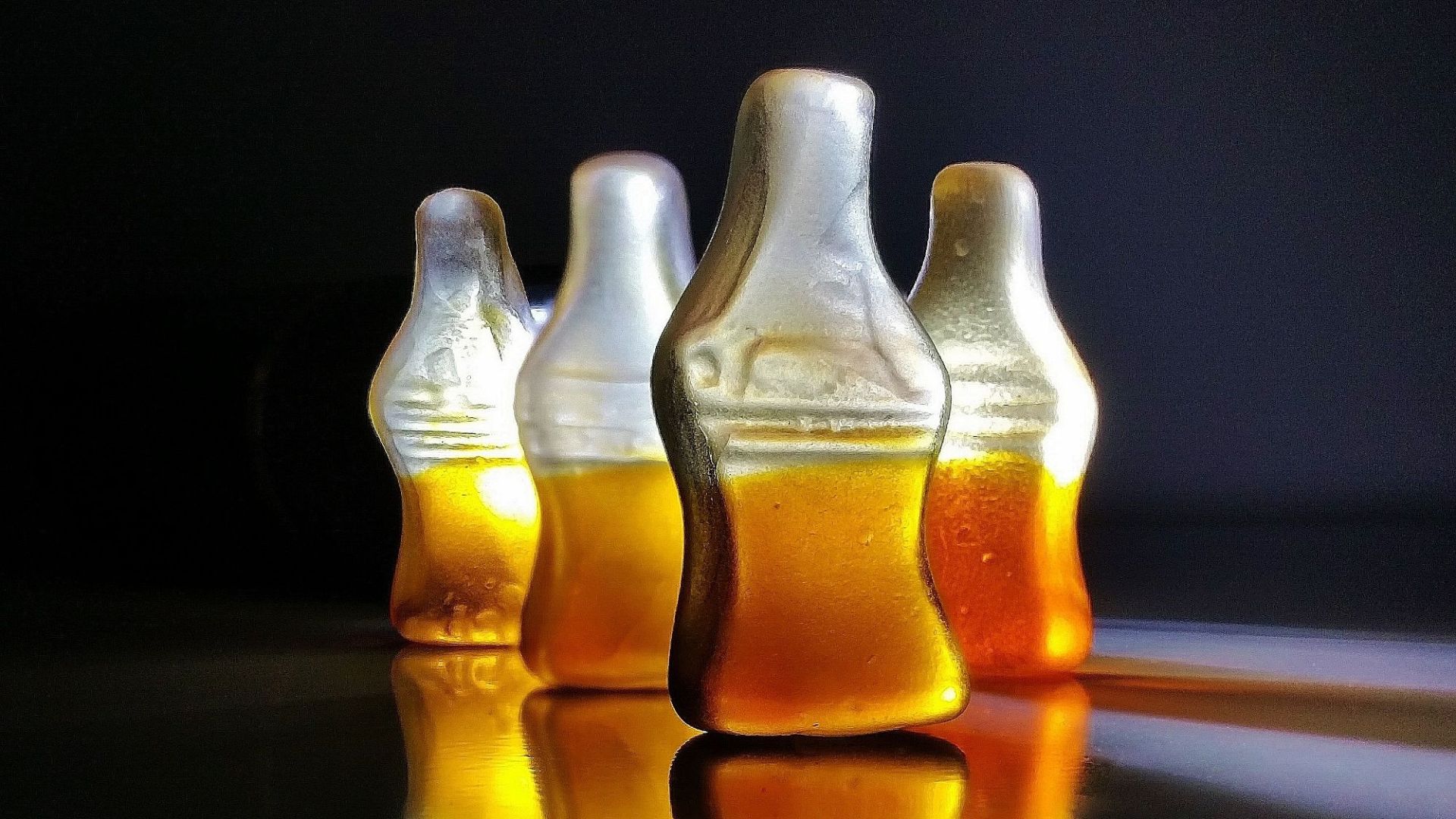 Close-up shot of cola-shaped gummy candies with reflections on a glossy surface.
