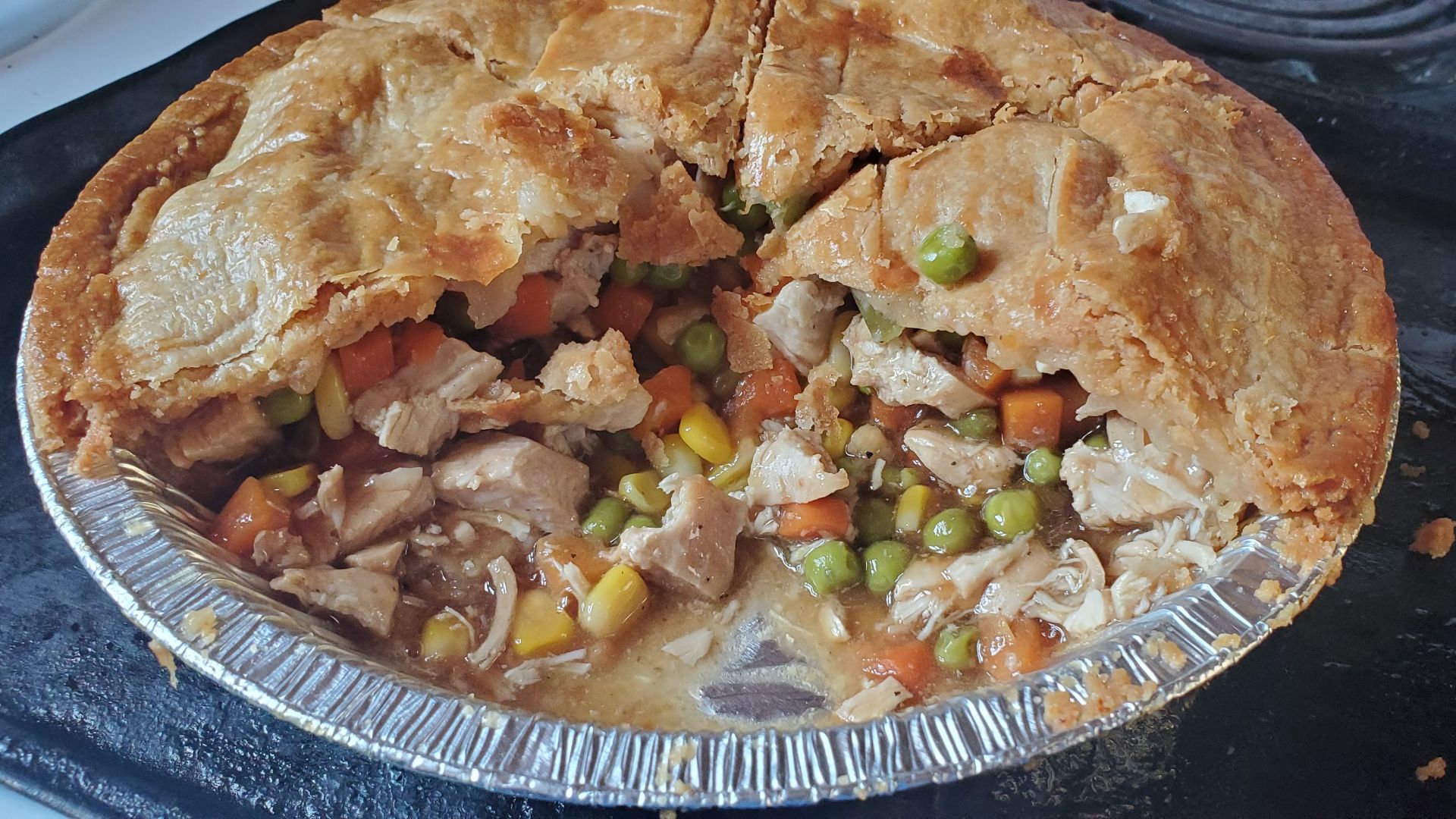 Homemade chicken, carrots, peas and corn pot pie in an aluminum pie plate on a baking sheet, cut open.