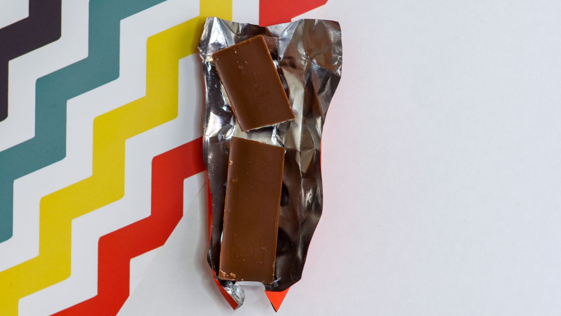 Chocolate bar unwrapped on vibrant zigzag background, showcasing bold design and indulgence.