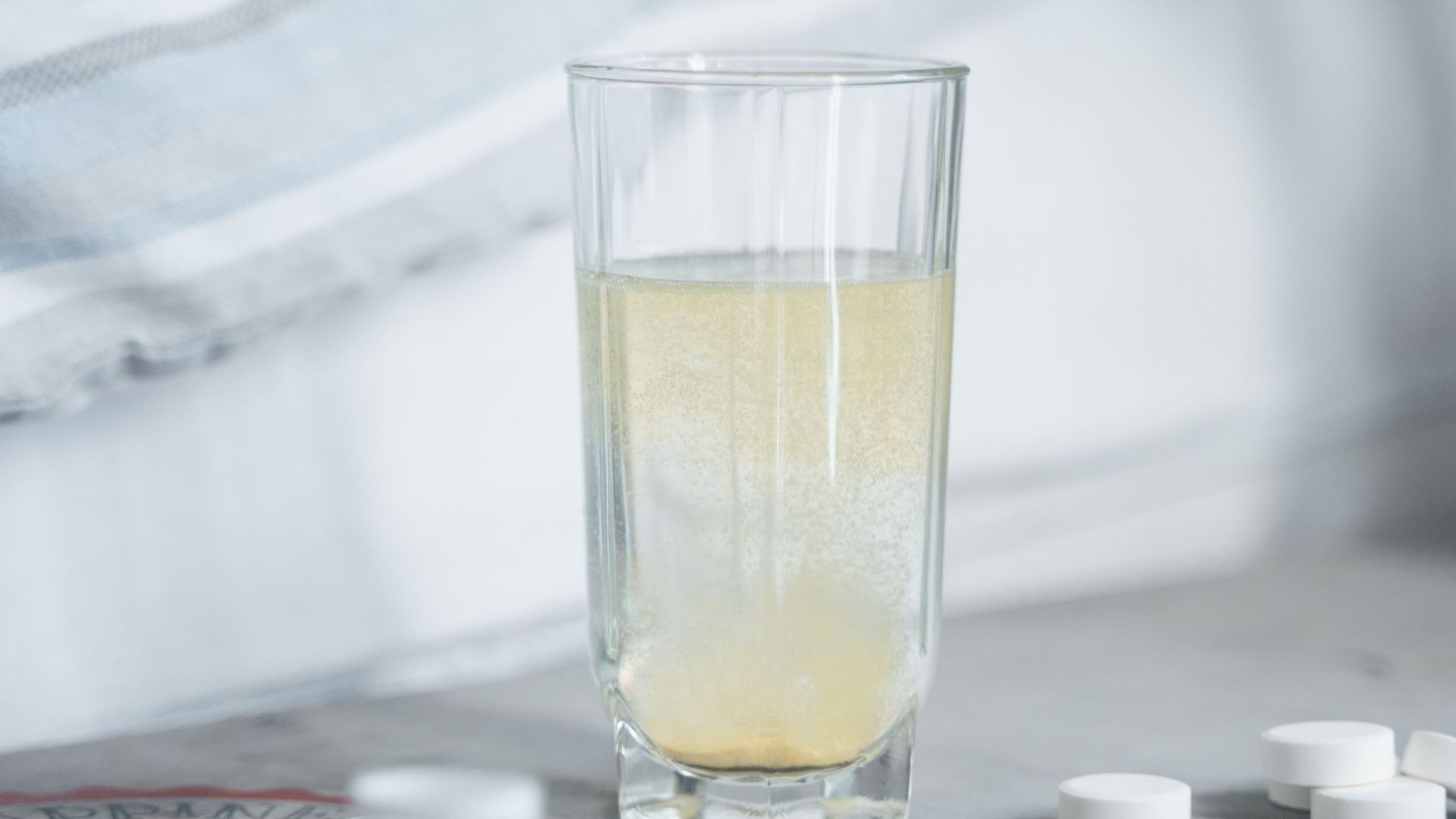 A close-up of an effervescent tablet dissolving in a glass of water on a bedside table.