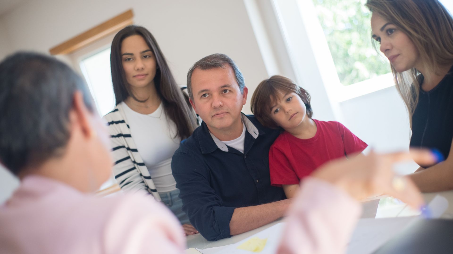 A family of four seeks advice from a professional during an indoor consultation in a bright room.