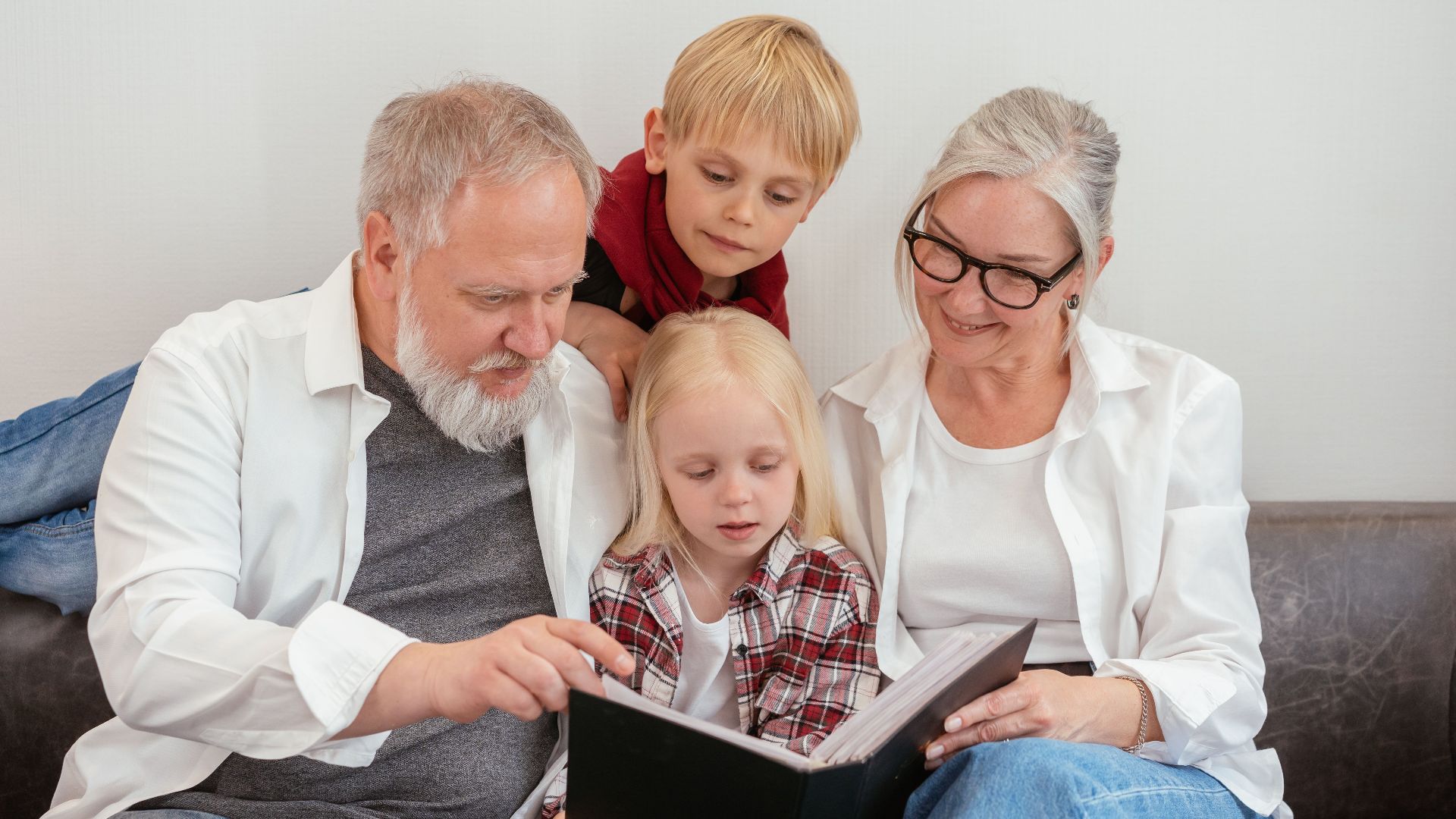 Grandparents and grandchildren reading a photo album on the couch, embracing family bonds and love.