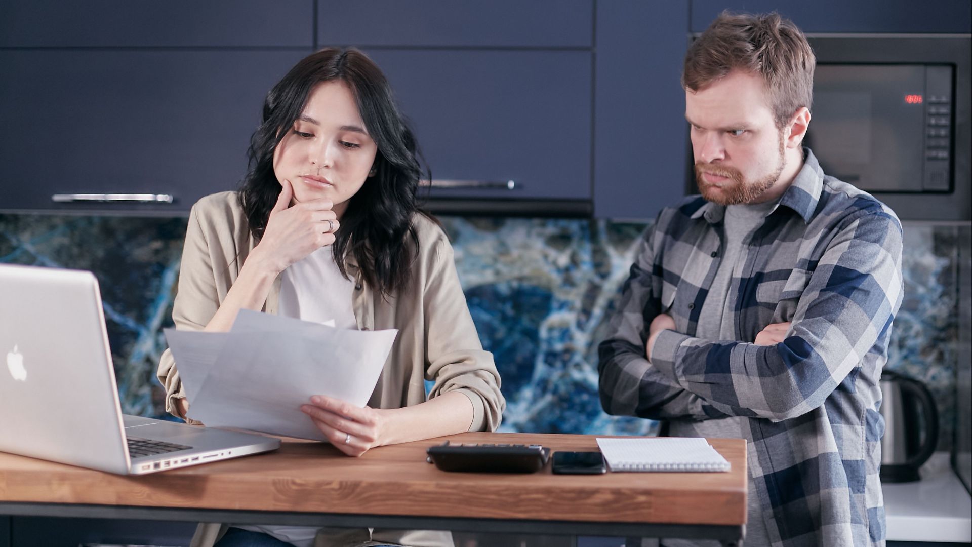 A couple sitting at a kitchen desk reviewing financial documents, using a laptop.