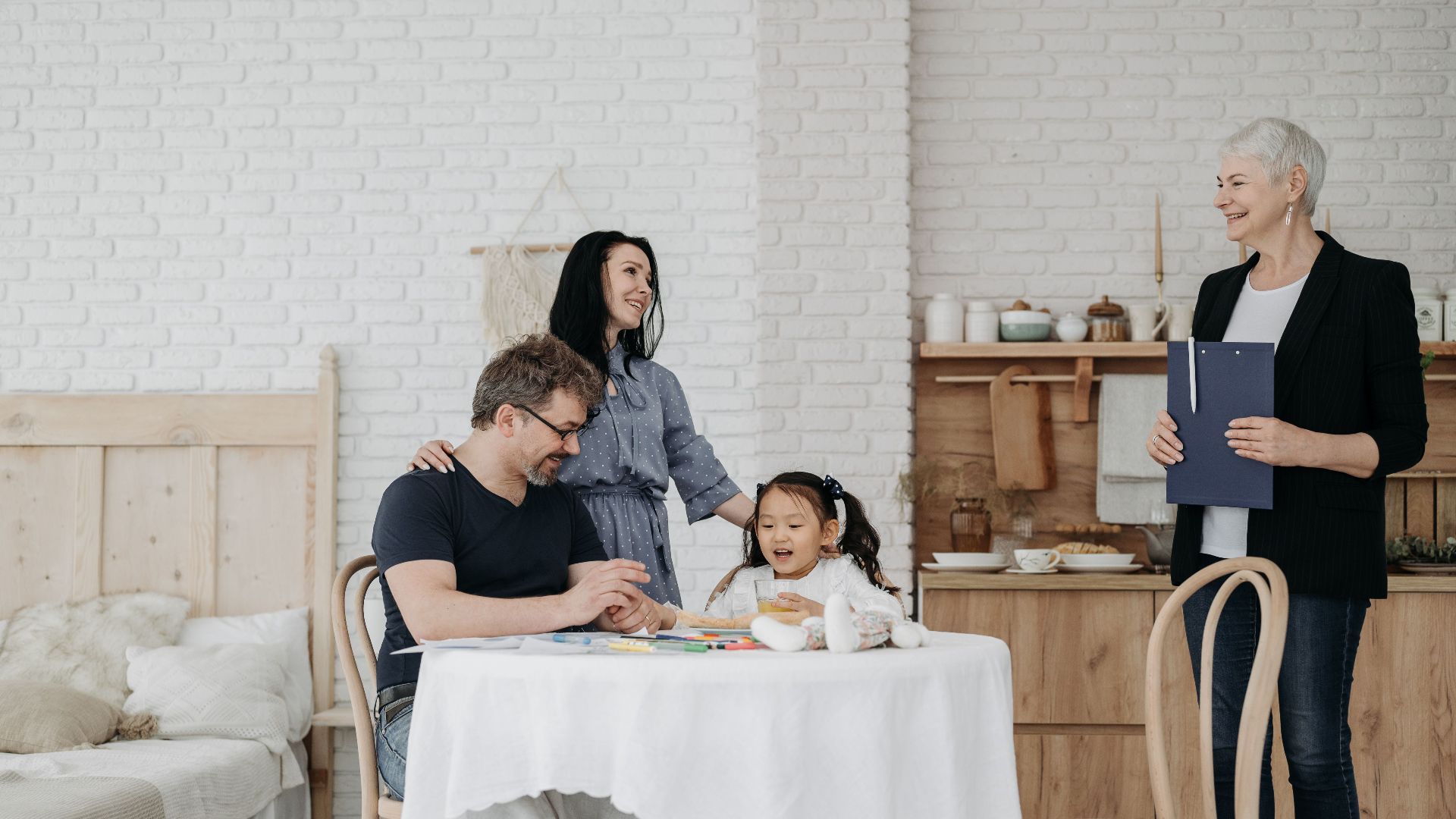 A happy family sits at a table with a child and social worker indoors, symbolizing adoption or foster care.