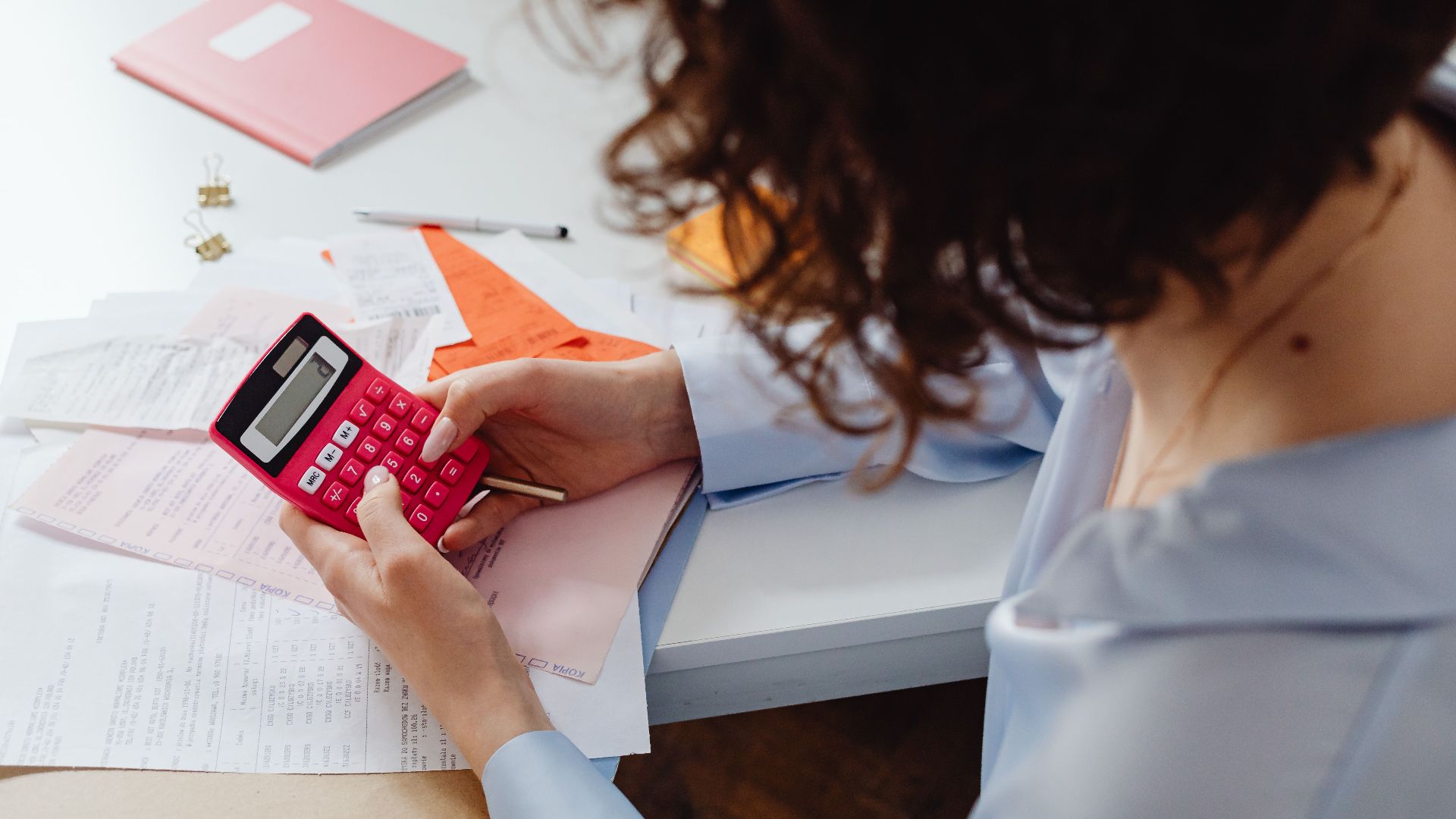Woman calculating expenses with documents and calculator at work desk.