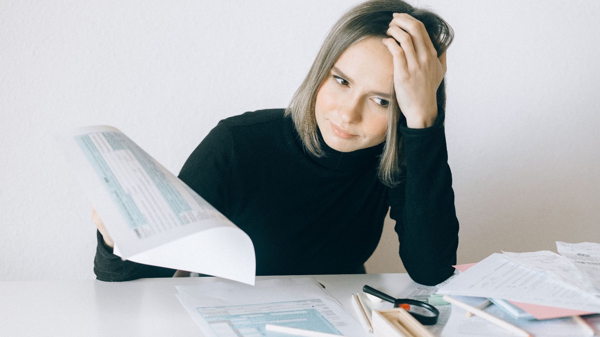 A woman showing stress while reviewing multiple paperwork and financial documents at a desk.