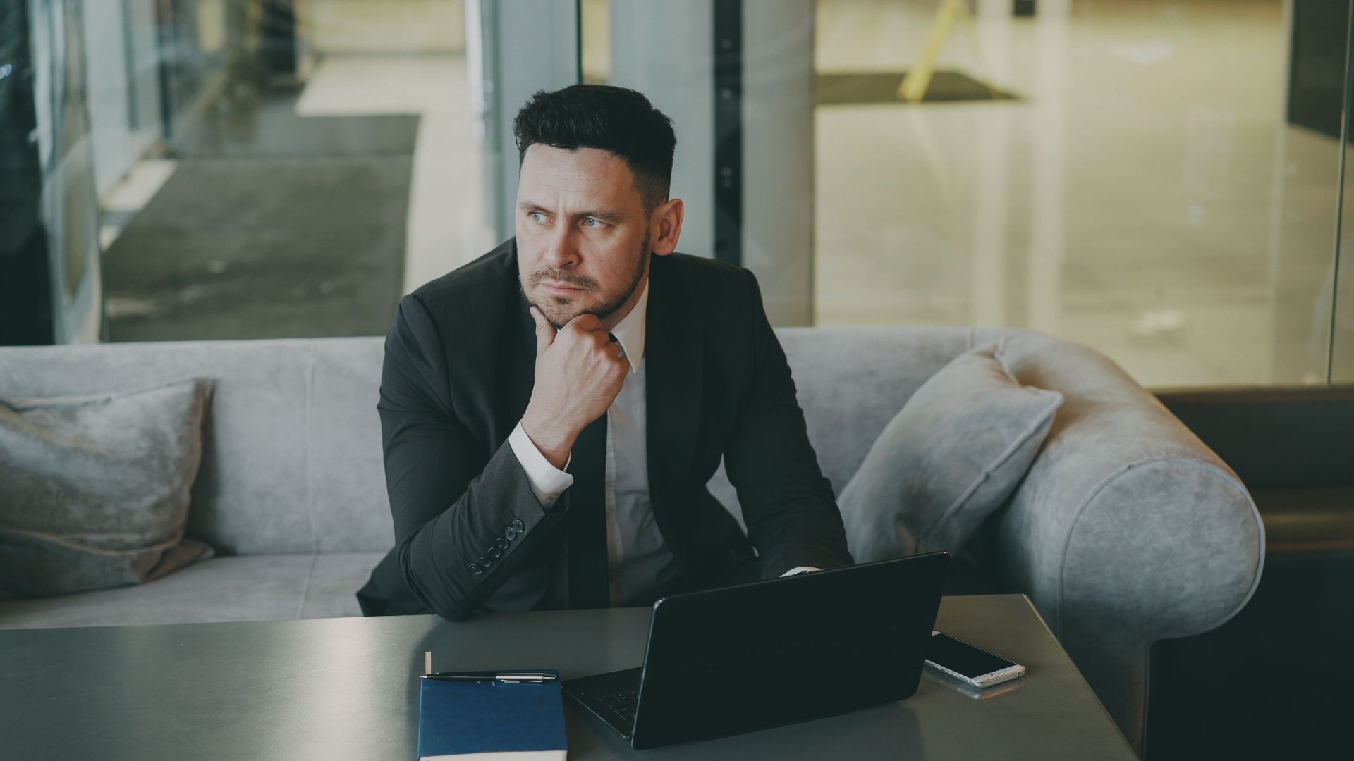 Professional businessman in suit pondering at desk in modern office lounge.