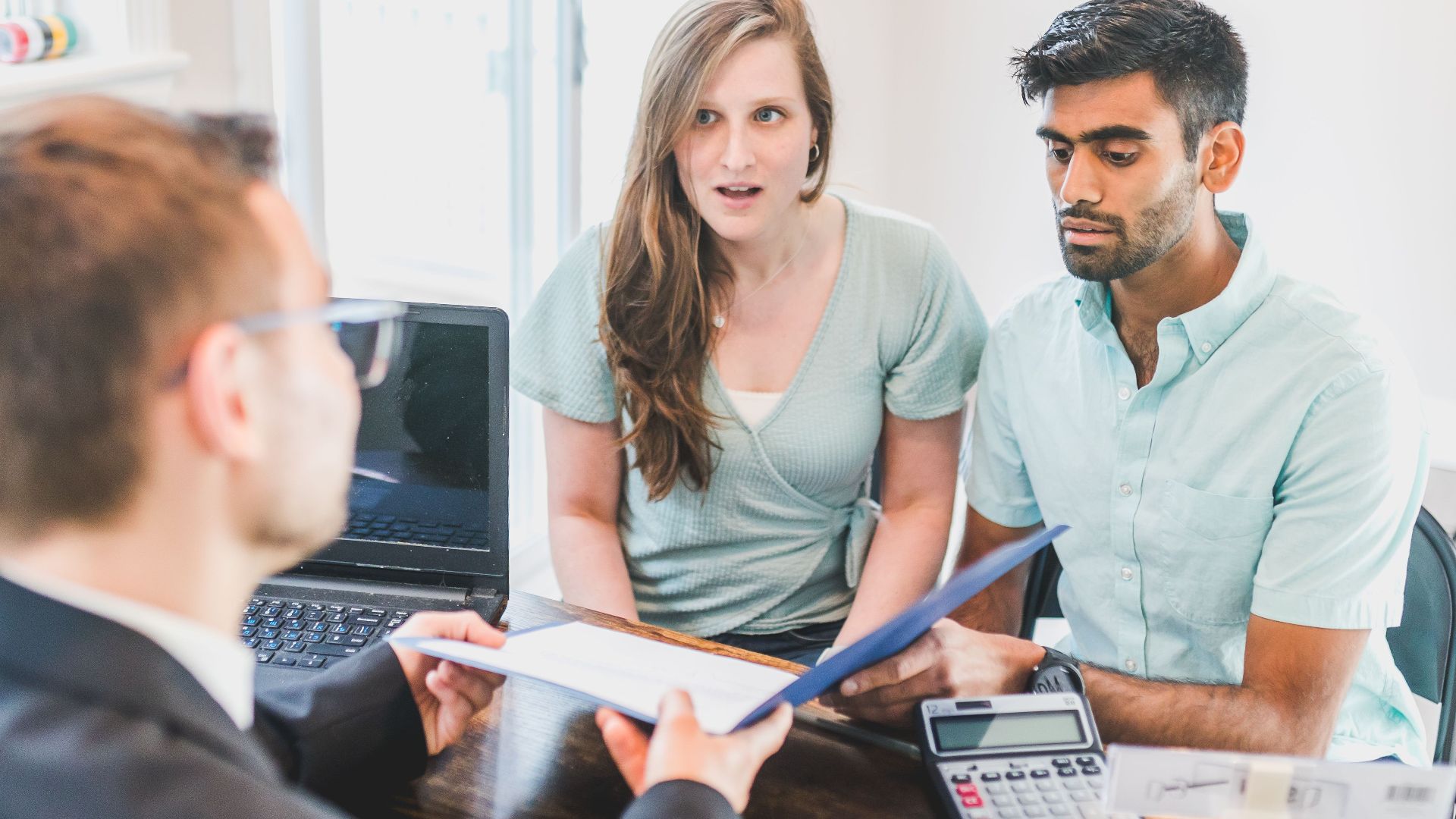A young couple discusses home buying options with a real estate agent indoors.