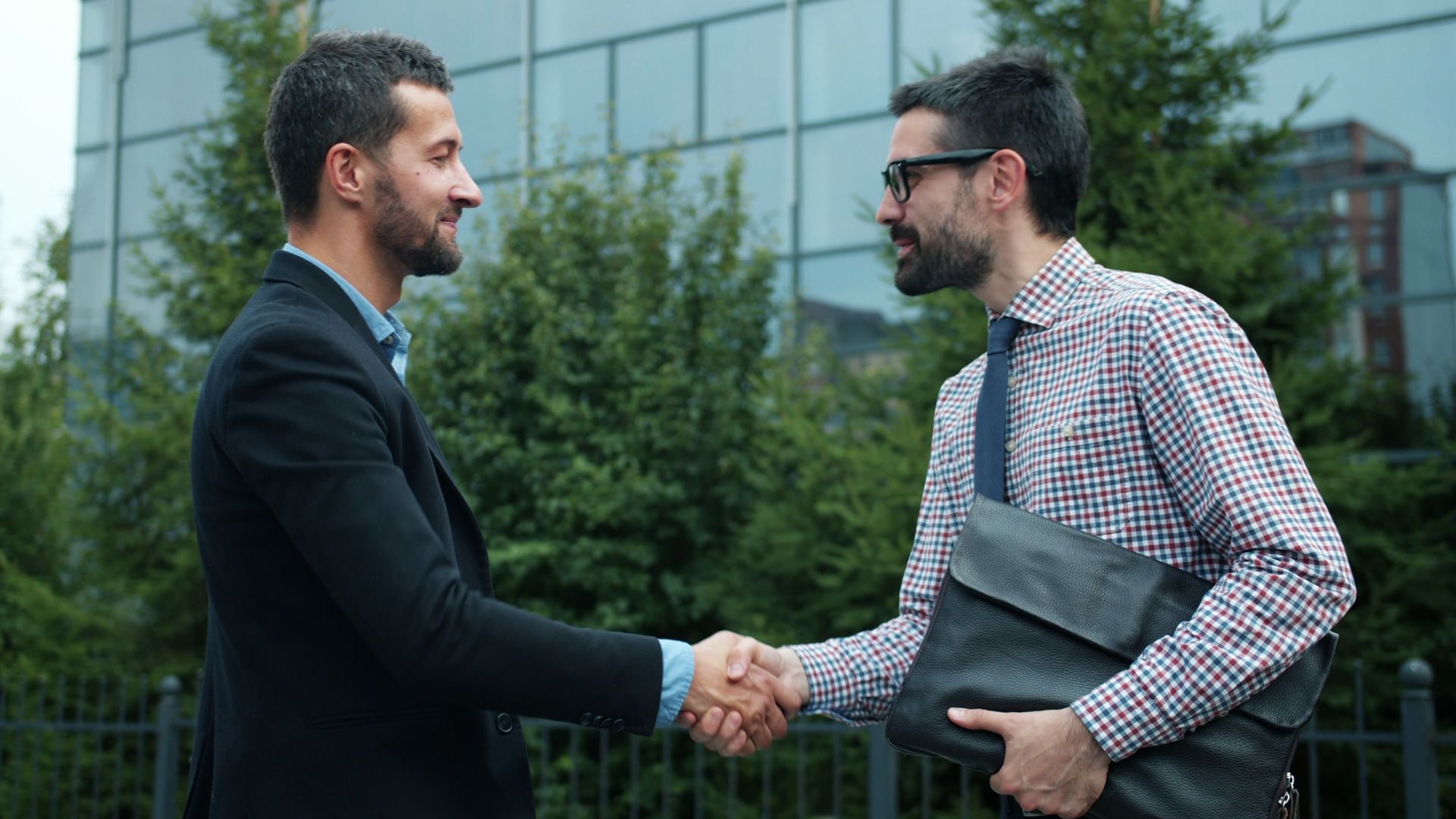Two businessmen shaking hands outside an office building, symbolizing partnership.