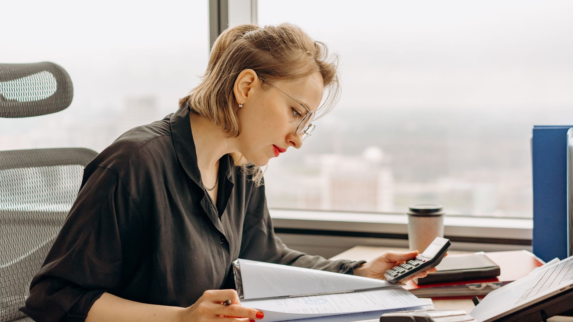 Woman accountant calculating financial documents at office desk.