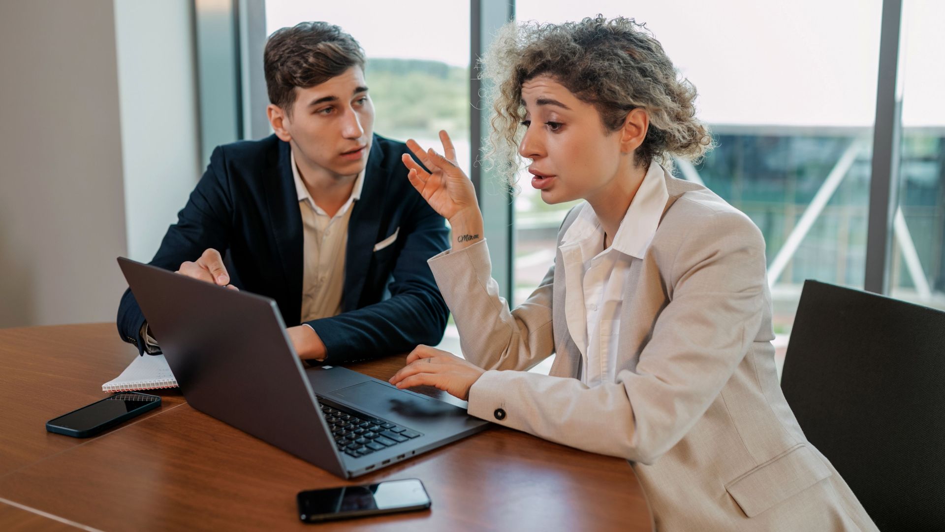 Two business professionals discussing ideas at a wooden table inside a modern office environment.