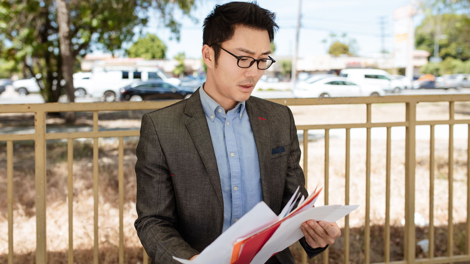 Asian businessman in a suit checking documents outdoors on a sunny day.
