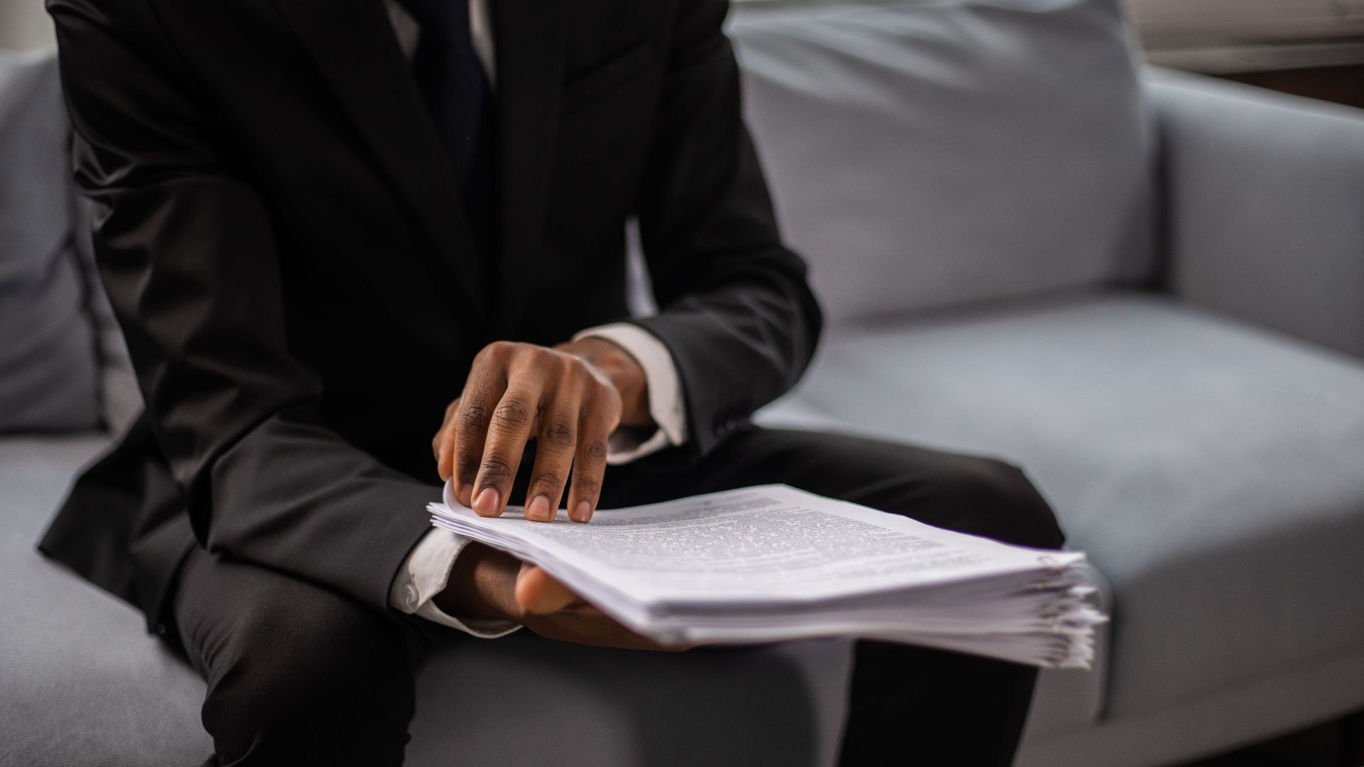 Close-up of a businessman in a suit reviewing documents while seated on a sofa indoors.