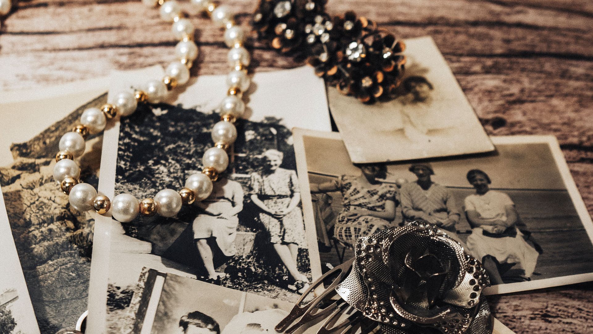 A collection of vintage black and white photos with pearl necklace and antique brooch displayed on a rustic wooden table.
