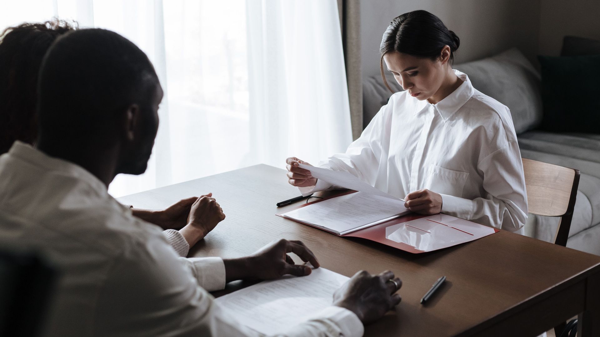 A professional woman reviews documents with a couple at home, indicating a collaborative decision-making process.
